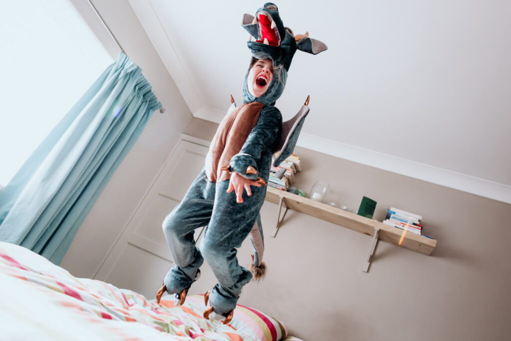 child in dragon costume jumping on a bed