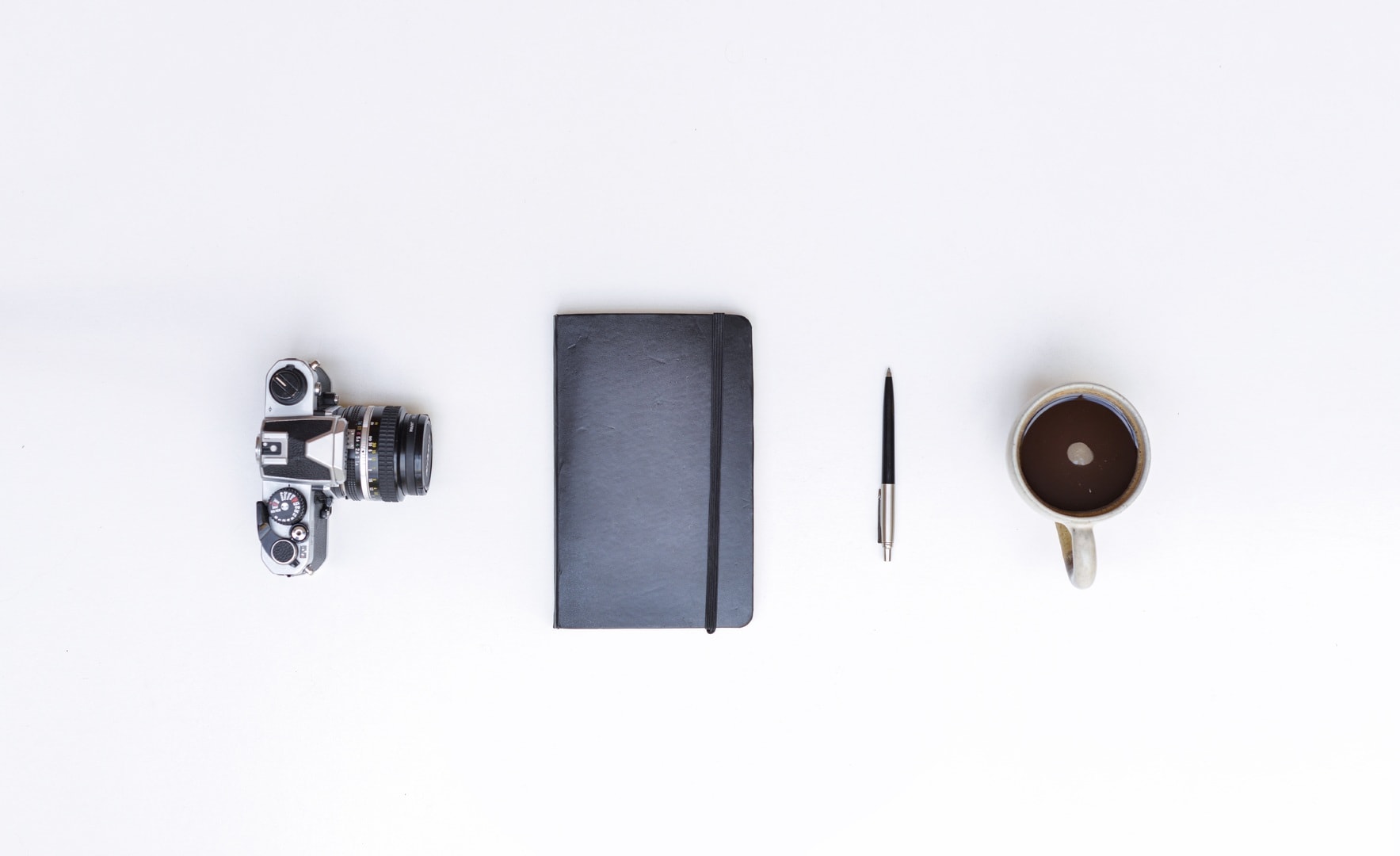 a camera, notebook, pen and coffee on a clean desk