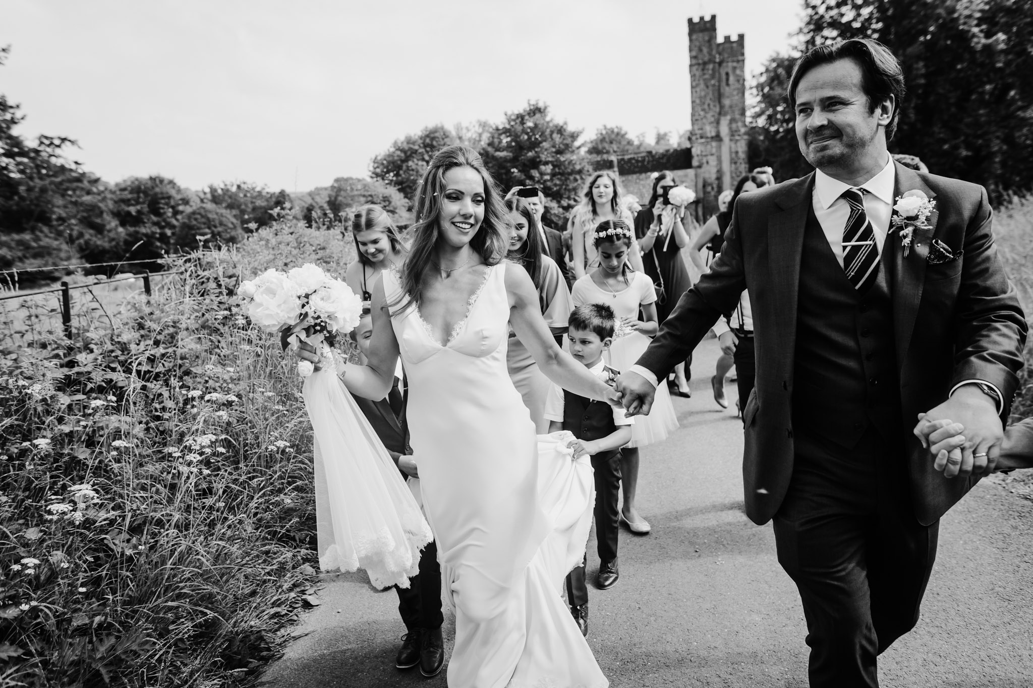 bride and groom walk to their reception with a parade of guests behind them huntsham court wedding