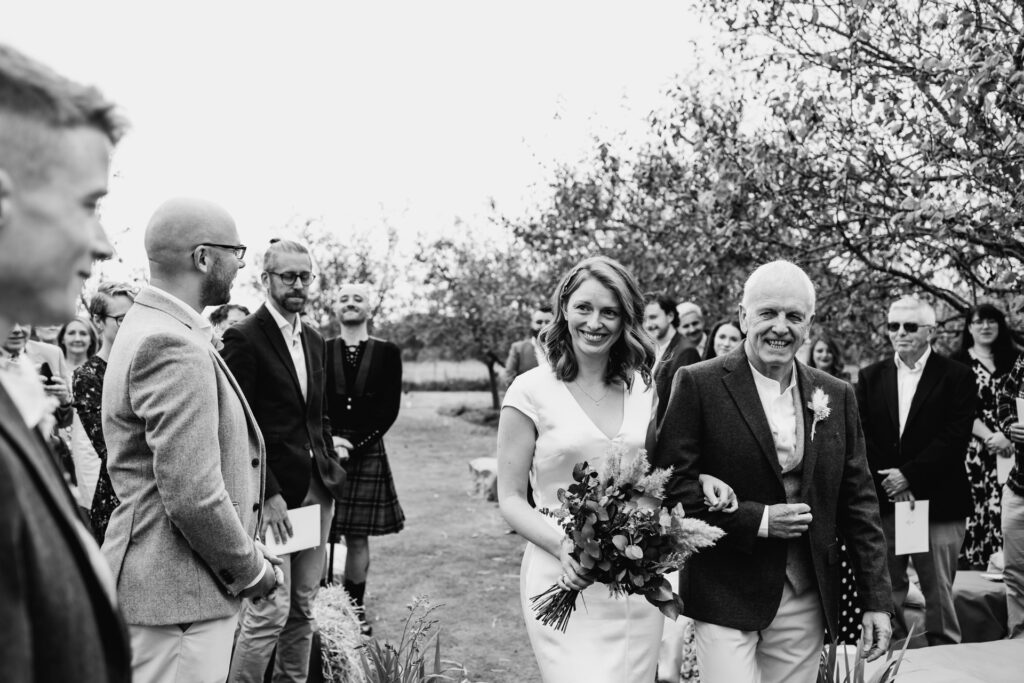 bride looks at husband to be as she walks down the aisle on the orchard