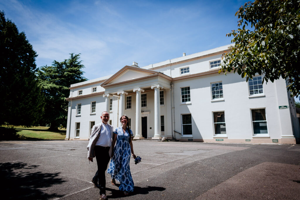 couple walk in front of follaton house on their way to wedding reception
