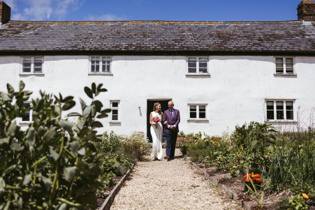 a fatther walks his daughter down the path at river cottage wedding