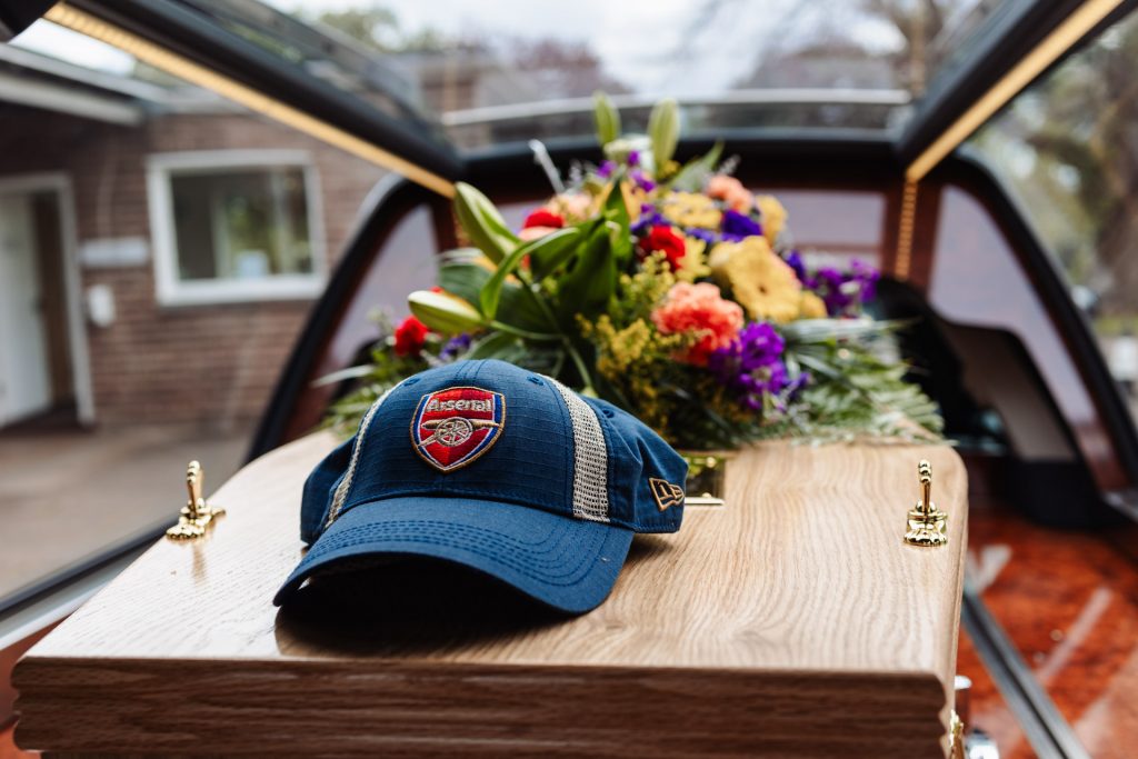 a coffin of a well loved man decorated with colourful flowers and his favourite football team hat at Exeter Crematorium