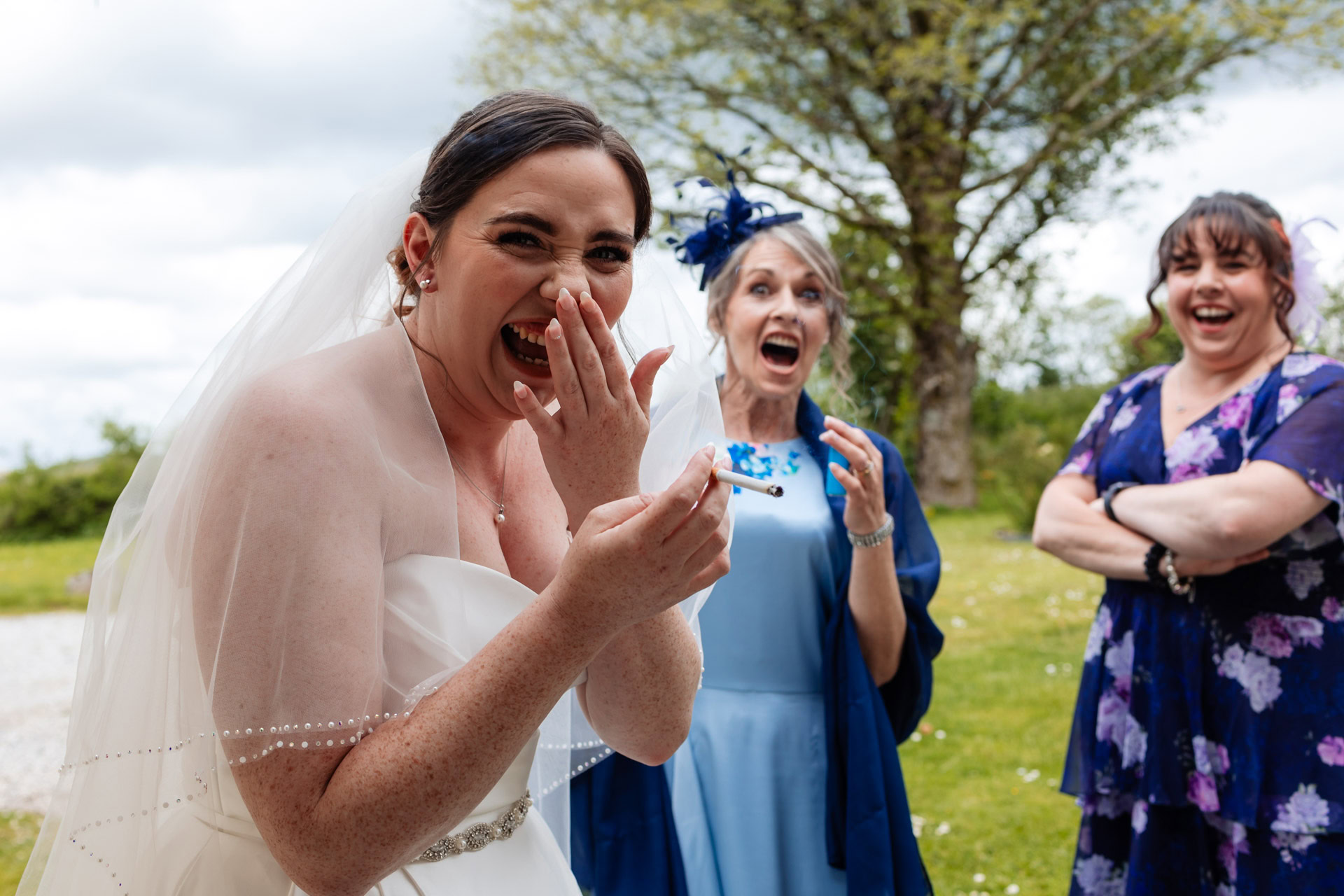 in true documentary wedding style a bride laughs while she is caught having a sneaky cigarette with the mums before her wedding