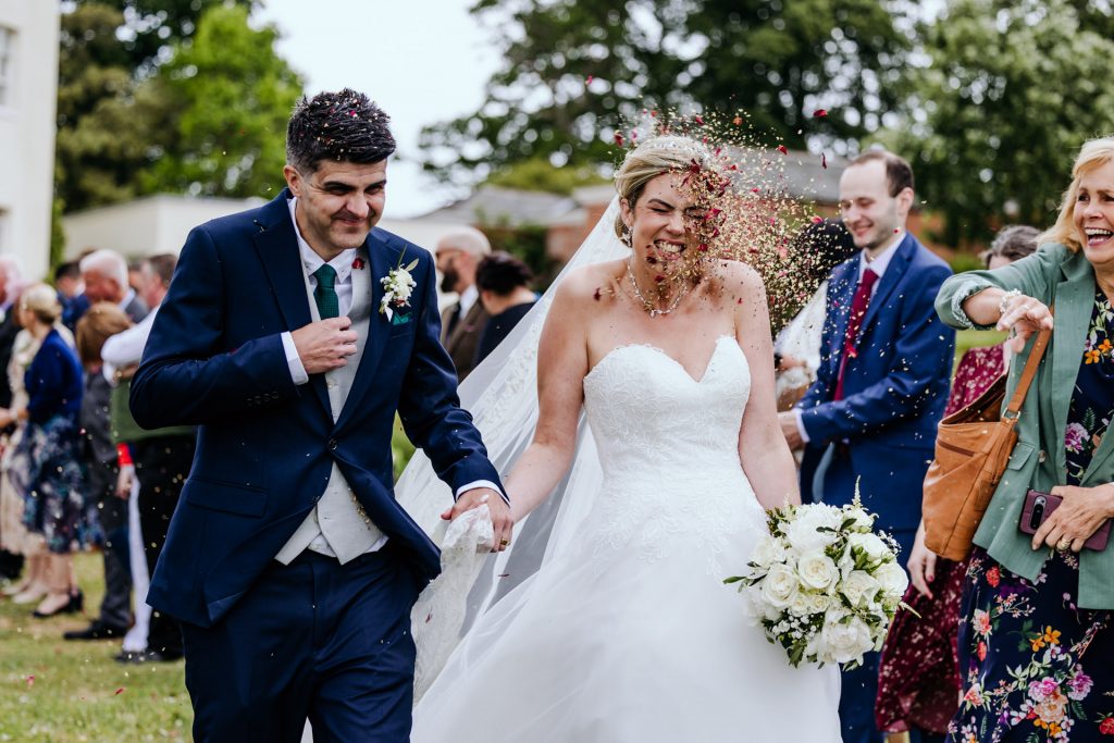 a bride gets pelted with natural petal confetti at a rockbeare manor wedding