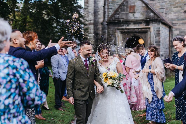 bride and groom huddle together as they get showered in confetti in tavistock