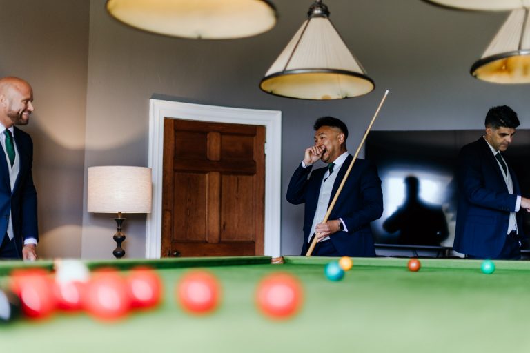 groomsman laughing while playing pool at rockbeare manor before the ceremony