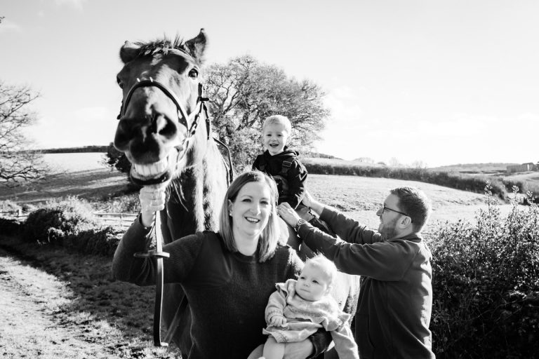 a family with toddler and newborn baby and their horse who seems to be laughing
