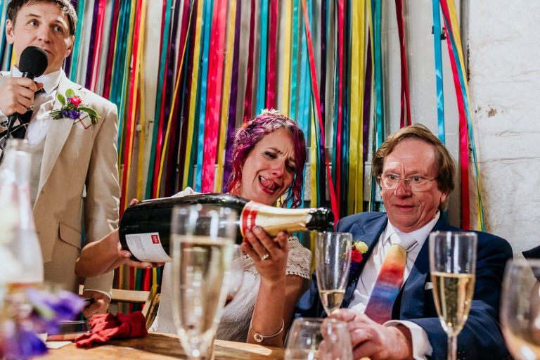 bride sticks her tongue out while pouring from a jeroboam of champagne