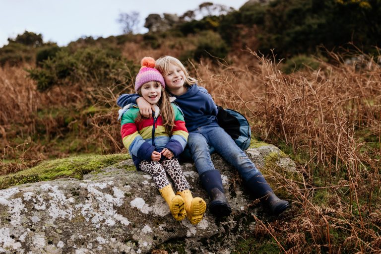 siblings sit on a rock and hug in a family day in the life session