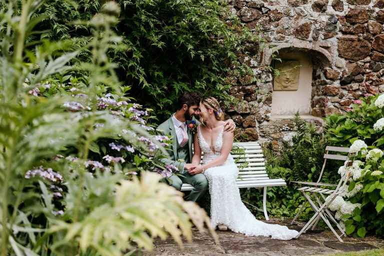 bride and groom snuggle on a bench in the gorgeous gardens at the great barn