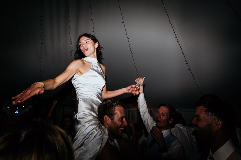 bride dancing up on guests shoulders at marquee wedding near Filleigh Devon