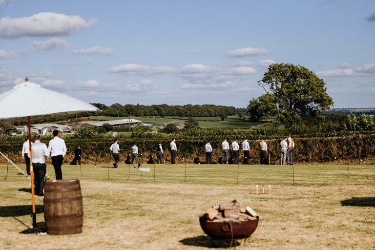 lots of male wedding guests peeing against a hedge after the speeches