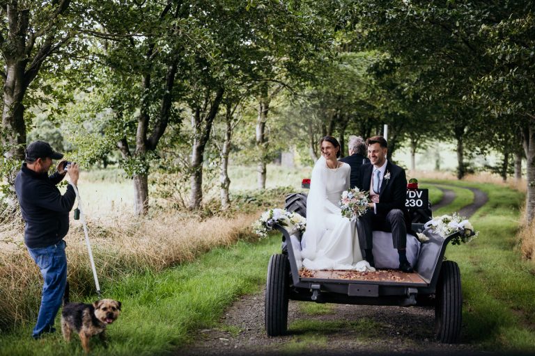 bride and grooom ride in a tractor trailer to their reception, watched by local dog walkers