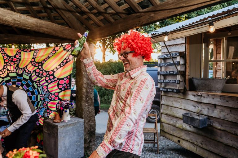 man in orange wig dances at a colourful festival style wedding