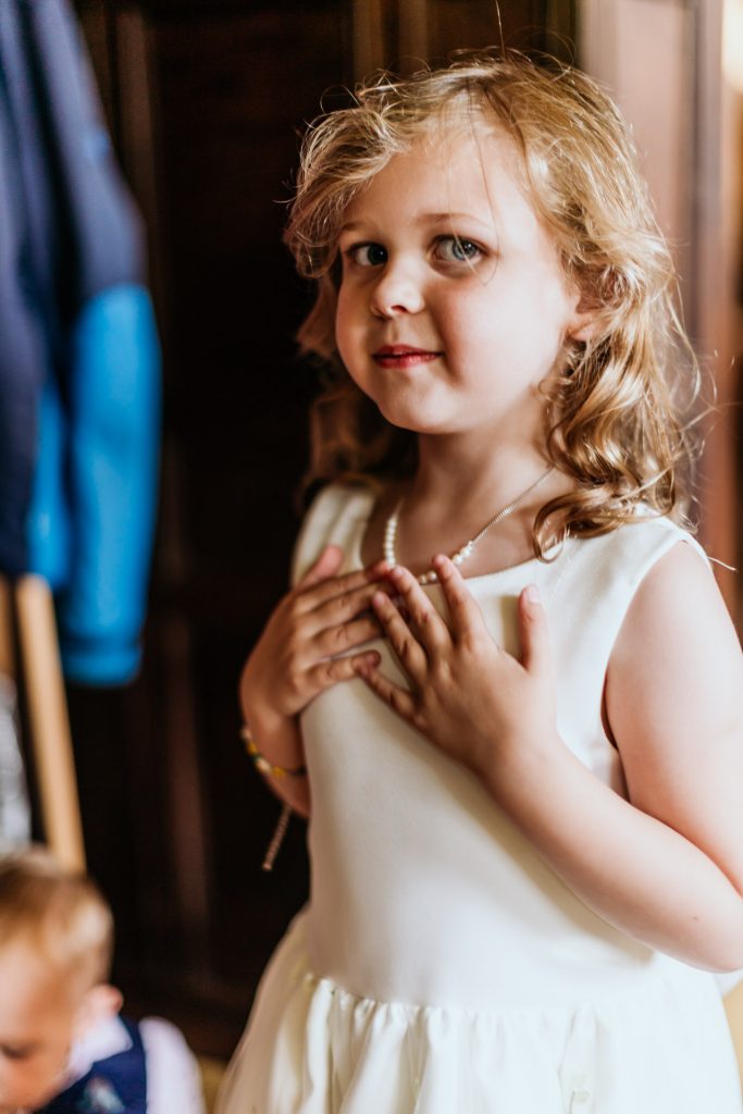 a young flower girl proudly puts her necklace on